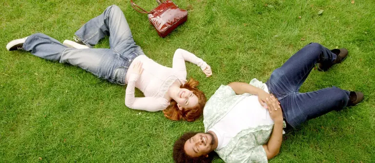 twee personen, vrouw met rood haar en man met zwarte krullen, liggen op het gras.