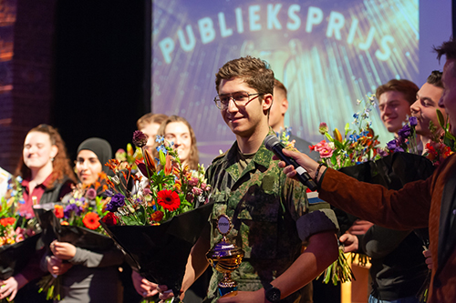 Lucas Frunt, Veva student van Yonder Groep mensen met bloemen, de middelst persoon houdt een trofee vast.
